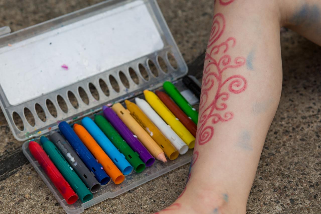 verschiedenfarbige Malfarben in einem Kasten und ein künstlerisch bemaltes Kinderbein.