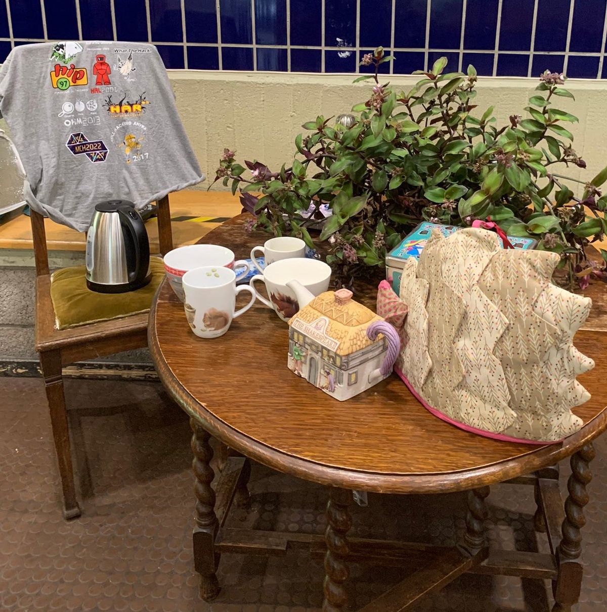 A wooden table and a chair with teamugs, a plant and a tea-pot